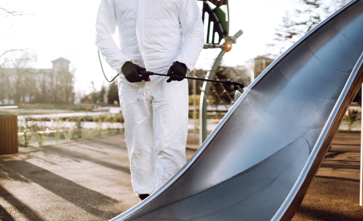 Osoba w kombinezonie ochronnym dokonuje czyszczenia konstrukcji stalowych na placu zabaw.