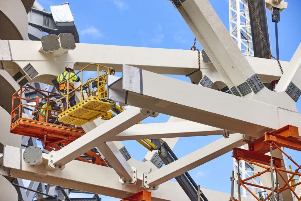 Robotnicy wykonują prace wysokościowe na podnośniku przy konstrukcji stalowej.